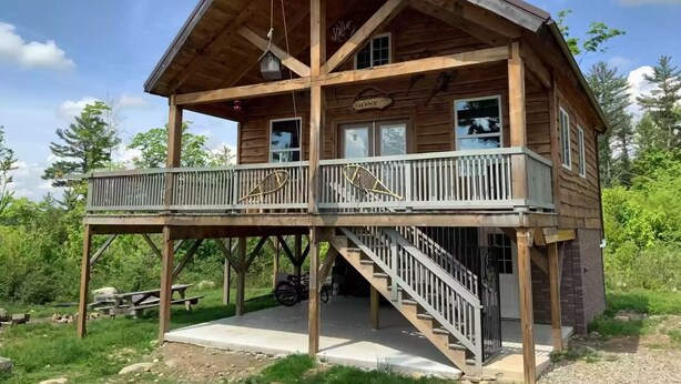Una cabaña de madera con balcón, una escalera y un cartel que dice "GONE".
