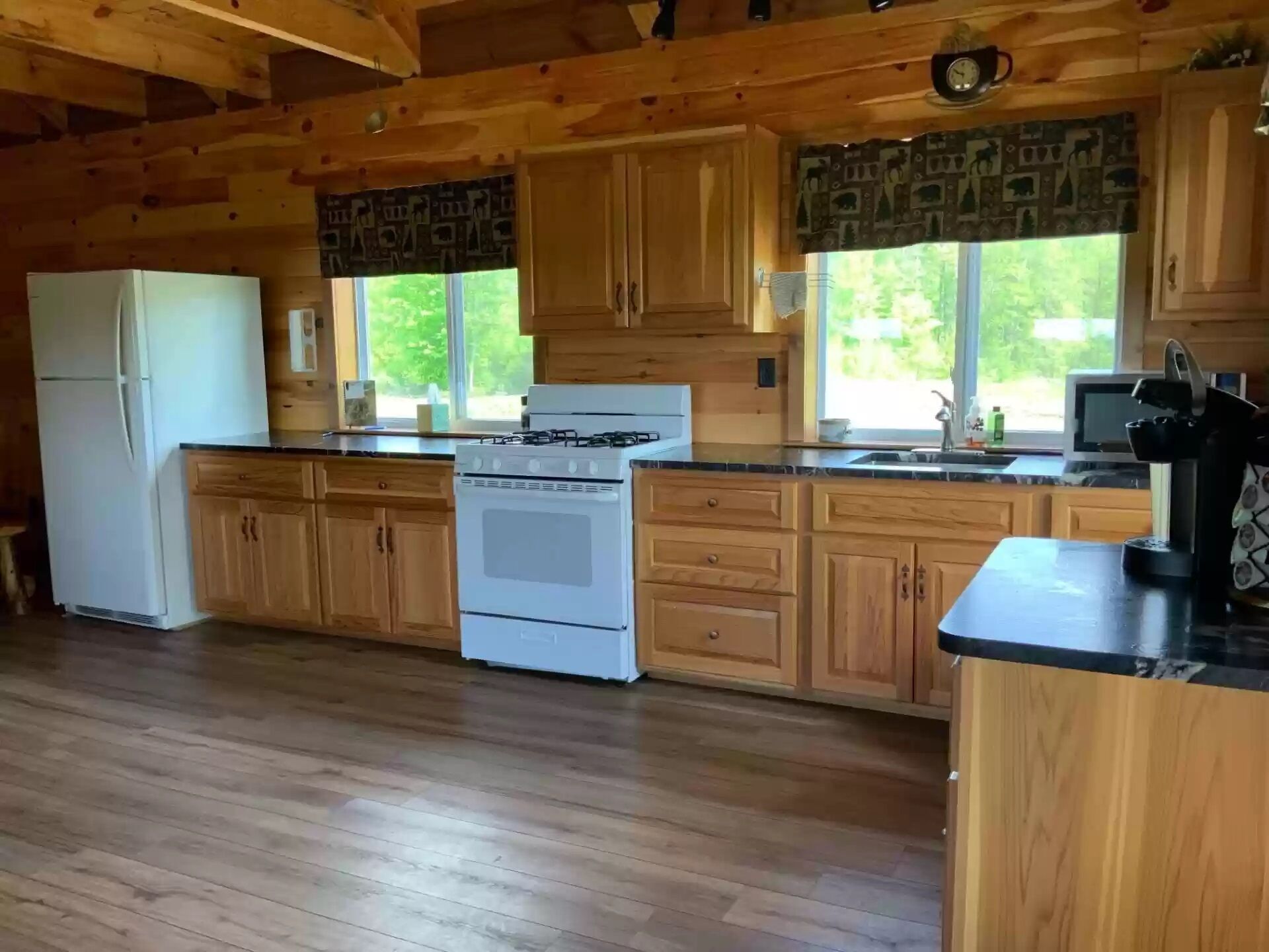 A kitchen with wooden cabinets, a stove, a refrigerator, and a window with a view of greenery.