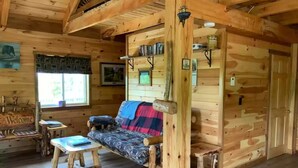 Interior acogedor de una cabaña con sofá, mesas de madera y un cartel que dice 'Welcome'.