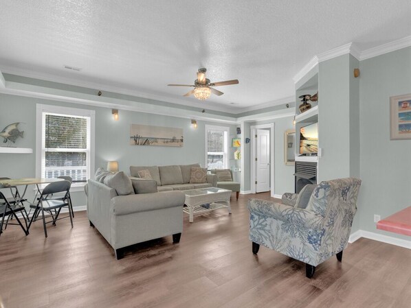 A spacious living room with a ceiling fan, a dining area with a table and chairs, and a kitchen area with a stove and cabinets.