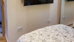 Ein Schlafzimmer mit einem Bett, einem an der Wand befestigten Fernseher und einem Spiegel.