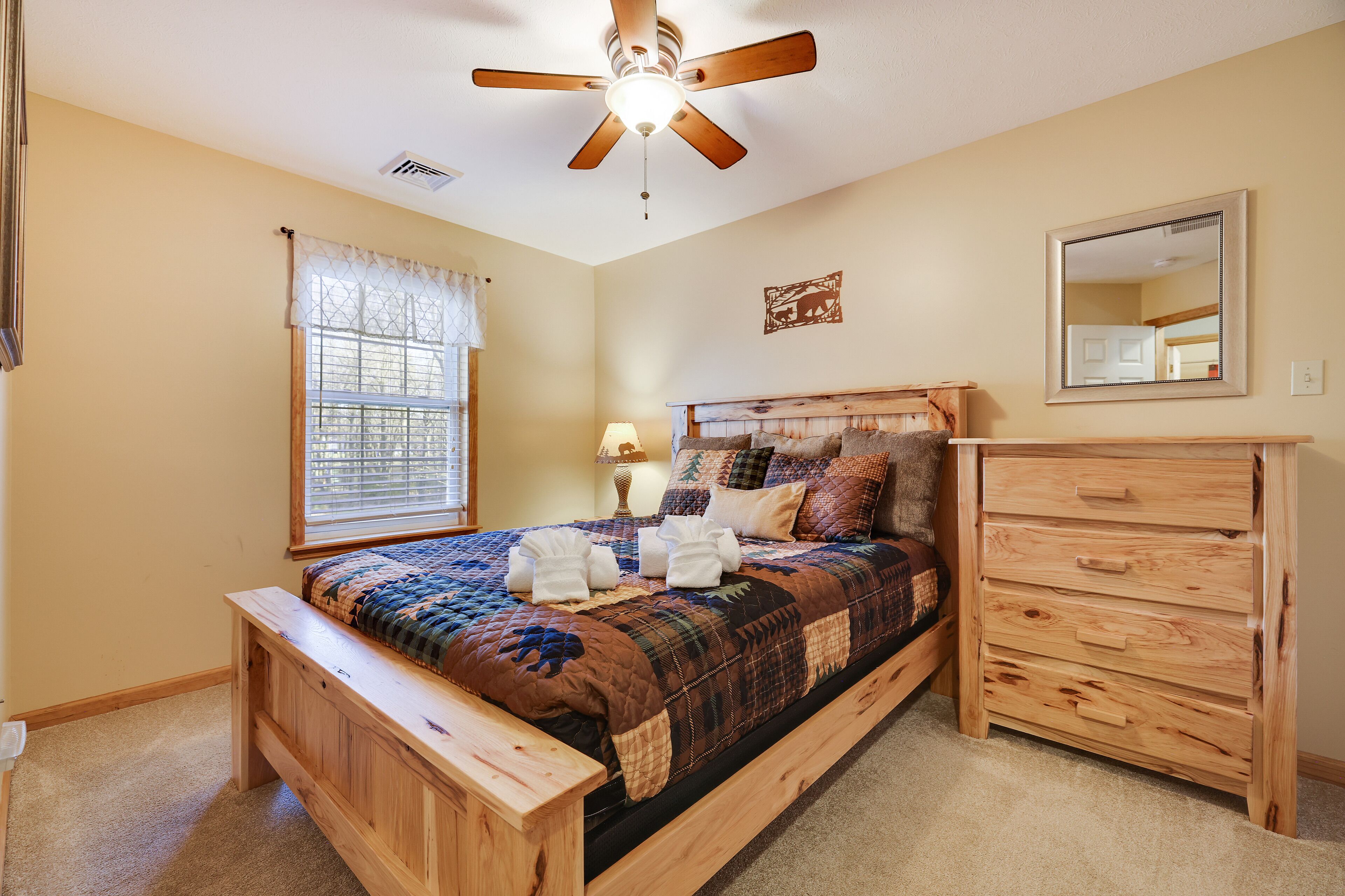 Une chambre à coucher avec un lit en bois, une table de chevet, une commode, un ventilateur de plafond et une fenêtre avec des rideaux.