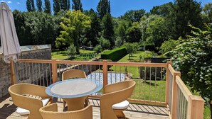 A deck with wicker furniture and a glass table, surrounded by a wooden railing and a stone wall. - Logis des Fées, spa, swimming pool, air conditioning & garden (Baugé en Anjou)