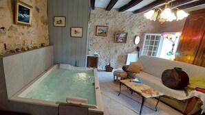 A rustic room with a large bathtub, a wooden table, and a sofa. - Logis des Fées, spa, swimming pool, air conditioning & garden (Baugé en Anjou)