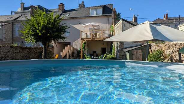 A swimming pool with clear blue water, surrounded by stone walls and a wooden deck. - Logis des Fées, spa, swimming pool, air conditioning & garden (Baugé en Anjou)