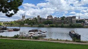 A riverside view with boats docked, a historic castle, and a church with twin spires in the background. - Logis des Fées, spa, swimming pool, air conditioning & garden (Baugé en Anjou)