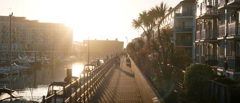 A waterfront promenade with a brick walkway, boats, and buildings with balconies.