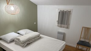 Una cama individual con sábanas blancas, una silla de madera, un radiador y una ventana con cortina.