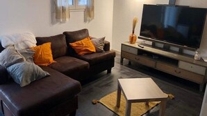 Una sala de estar con un sofá de cuero marrón, una mesa de centro blanca y un televisor de pantalla plana sobre un soporte de madera.