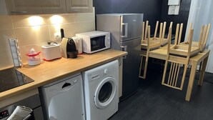 Cocina compacta equipada con lavavajillas, lavadora, microondas y refrigerador. Hay sillas de madera y una mesa pequeña.