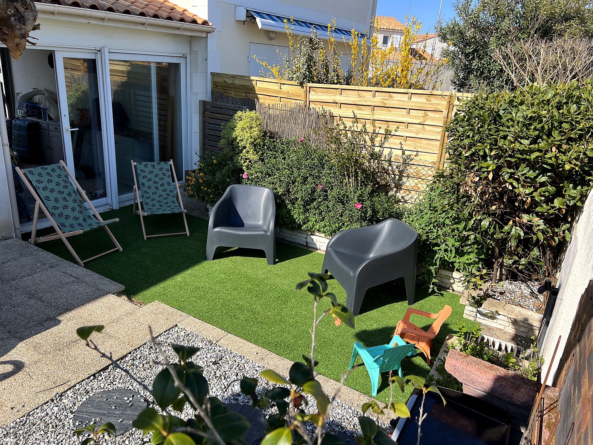 A backyard with artificial grass, a patio area with seating, and a wooden fence.