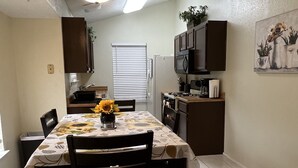 A dining area with a table set for four, a kitchen in the background, and a window with blinds. - Cheerful 2 Bedroom Home w/Parking in Central South Austin Pet Stays for Free ! (Austin)