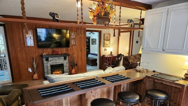 A bar area with a stone fireplace, wooden bar counter, and three stools.