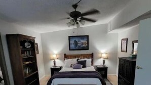 A bedroom with a bed, bedside tables, a ceiling fan, a bookshelf, and a patterned rug.