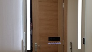 A bathroom with a wooden door, a mirror, a sink, and a bottle of shampoo.