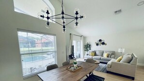 A modern living room with a wooden dining table, a sofa set, and a chandelier. - Renovated villa w private pool & bbq - close to magic theme parks!! (Davenport)