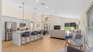 A modern kitchen with a central island, bar stools, and a dining area with a table and chairs. - Renovated villa w private pool & bbq - close to magic theme parks!! (Davenport)