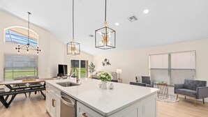 A modern kitchen with a large island, pendant lights, and a dining area with a bench. - Renovated villa w private pool & bbq - close to magic theme parks!! (Davenport)