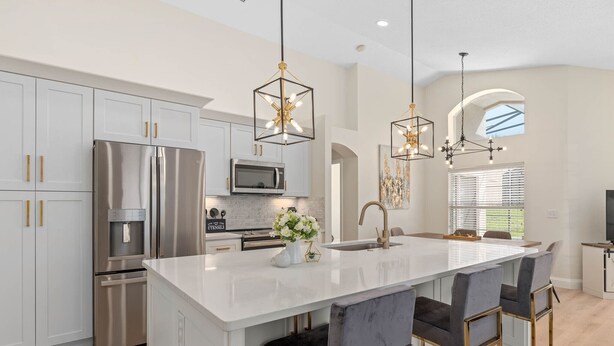 A modern kitchen with white cabinets, stainless steel appliances, and a central island with bar stools. - Renovated villa w private pool & bbq - close to magic theme parks!! (Davenport)
