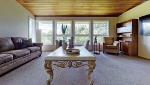 Una sala de estar con un sofá de cuero marrón, una mesa blanca con adornos, una silla de madera y una estantería.