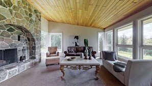 Una sala de estar acogedora con chimenea de piedra, techo de madera y ventanas amplias que ofrecen vistas al exterior.