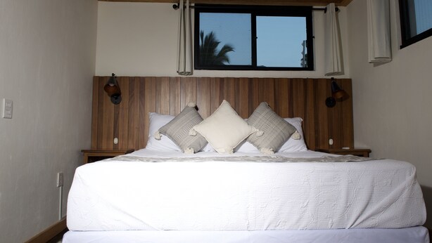 A bedroom with a wooden headboard, a large window with curtains, and a bed with white bedding and multiple pillows. - Lake Front (Ajijic)