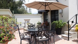 An outdoor patio with a round table and chairs, surrounded by potted plants and a large umbrella. - Lake Front (Ajijic)