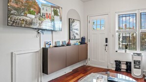 A modern living room with a large flat-screen TV mounted on the wall, a wooden cabinet, a door with a window, and a radiator.