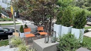 An outdoor seating area with two orange chairs and a table, surrounded by potted plants and a concrete planter.