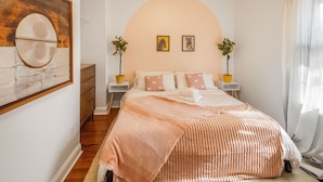 A bedroom with a large bed, a wooden headboard, two bedside tables with lamps, and wall art.