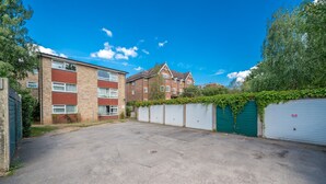 A residential area with a paved driveway, a row of garages, and a brick building with a red facade. - Spacious Pet Friendly 2-bed Apartment in Redhill (Redhill)