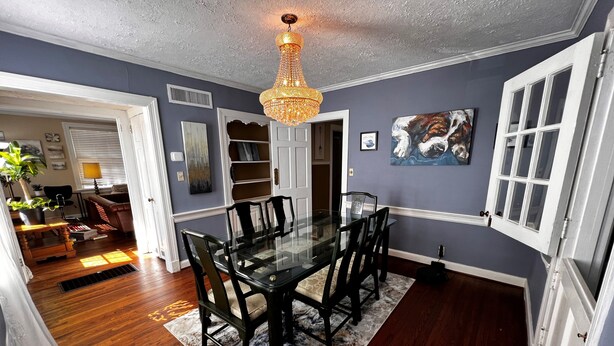 A dining area with a glass table and chairs, a chandelier, and a painting on the wall. - Historic 3-bedroom Cloverdale Home next to Playhouse (Montgomery)
