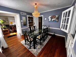 A dining area with a glass table and chairs, a chandelier, and a painting on the wall. - Historic 3-bedroom Cloverdale Home next to Playhouse (Montgomery)