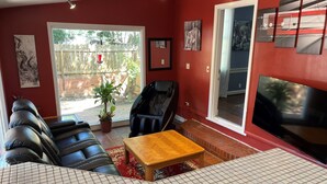 A living room with a red wall, a black leather sofa, a wooden coffee table, a TV, and a large window. - Historic 3-bedroom Cloverdale Home next to Playhouse (Montgomery)
