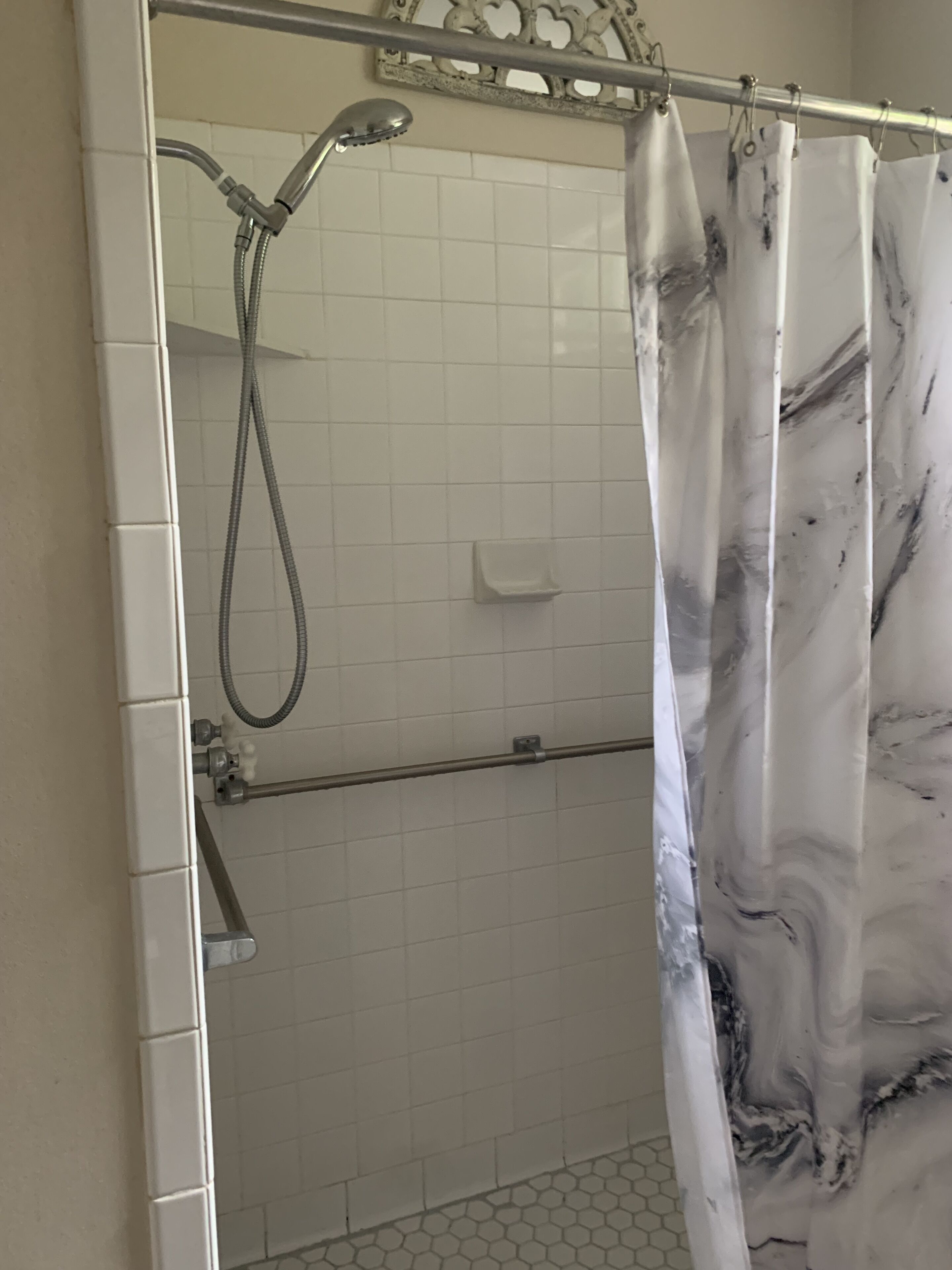 Un espace douche doté d’une porte en verre, d’un pommeau de douche à main et d’un rideau de douche à motifs de marbre.