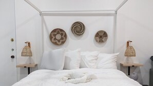 A white bedroom with a queen-sized bed, three woven wall art pieces, two bedside lamps, and a white duvet. - Charming Studio Condo Steps From Beach - Sleeps 4 (Myrtle Beach)
