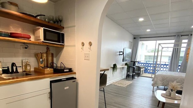 A modern kitchen with white cabinets, a microwave, and a dishwashing unit. There is a wooden floor and a small rug near the entrance. - Charming Studio Condo Steps From Beach - Sleeps 4 (Myrtle Beach)