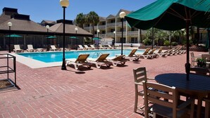 A poolside area with lounge chairs and umbrellas, a brick patio, and a building with balconies in the background. - Charming Studio Condo Steps From Beach - Sleeps 4 (Myrtle Beach)