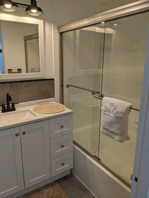 A modern bathroom with a glass shower enclosure, a white sink with a round mat, and a mirror above the sink. - Charming Studio Condo Steps From Beach - Sleeps 4 (Myrtle Beach)