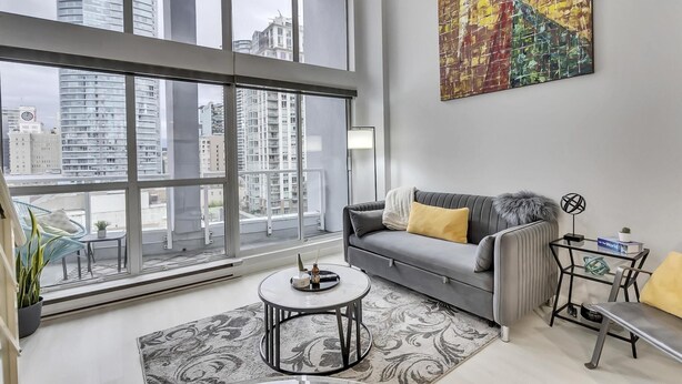 A modern living room with a gray sofa, a round coffee table, and a large window offering a city view. - Modern Downtown Vancouver Loft. Parking included.  (Vancouver)