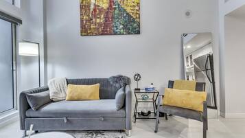 A modern living room with a grey sofa, two yellow cushions, a coffee table, and a large abstract painting on the wall.