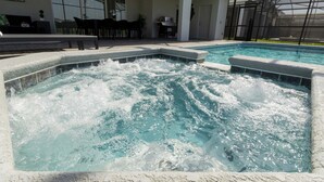 Une piscine avec un jacuzzi, un espace salon extérieur et une terrasse couverte.