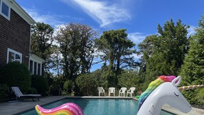 Une piscine avec un flotteur en forme de licorne, entourée d’arbres et d’une maison.