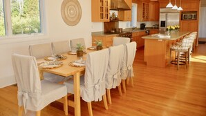 Une cuisine moderne avec des meubles en bois, un îlot central doté de tabourets de bar et un coin repas avec une table et des chaises en bois.