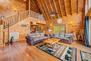 Cozy cabin interior with a high ceiling, exposed beams, and a comfortable seating area featuring a large sectional sofa and wooden coffee table.