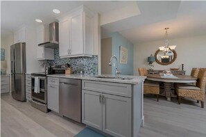 Enjoy cooking in the well-equipped kitchen with a refrigerator, oven, and dishwasher, and dine in the adjacent dining area with a round table and wicker chairs.