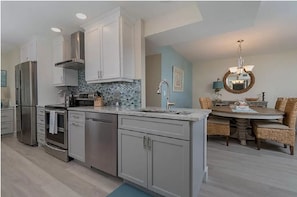 Enjoy cooking in the well-equipped kitchen with a refrigerator, oven, and dishwasher, and dine in the adjacent dining area with a round table and wicker chairs.