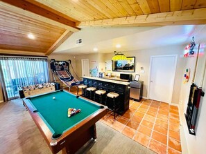 A cozy room with a pool table, foosball table, and a bar area.