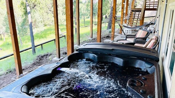 Ett bubbelbad fyllt med vatten, omgivet av trädäckstolar och en överbyggd sittgrupp, med utsikt över ett grönskande landskap.