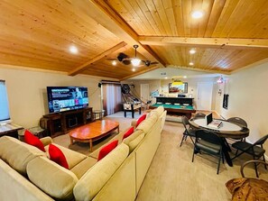 A cozy living room with a wooden ceiling, a large TV, a foosball table, and a pool table.